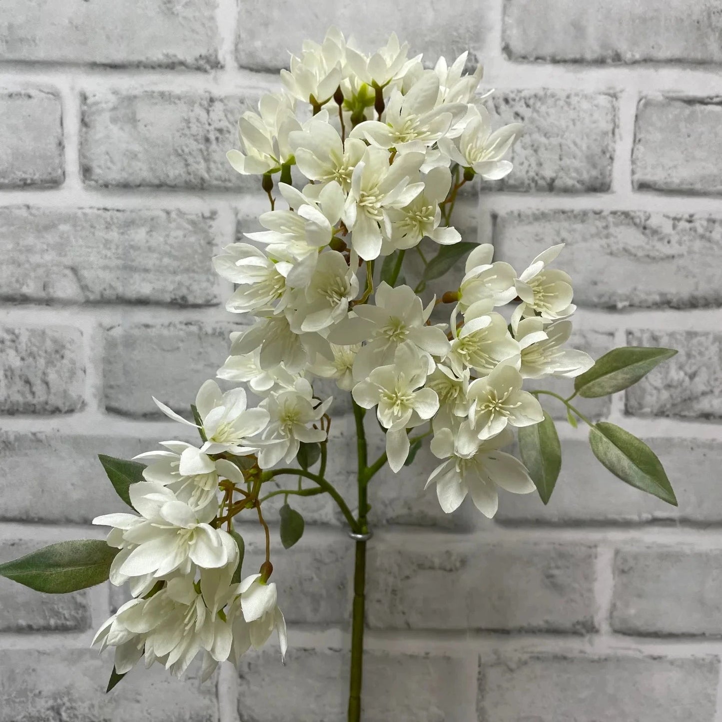 Artificial white flower arrangement against a gray brick wall