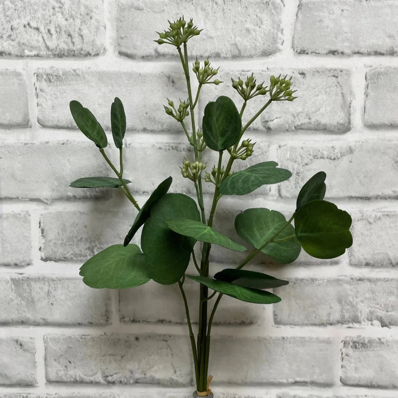 Artificial green plant against a white brick wall
