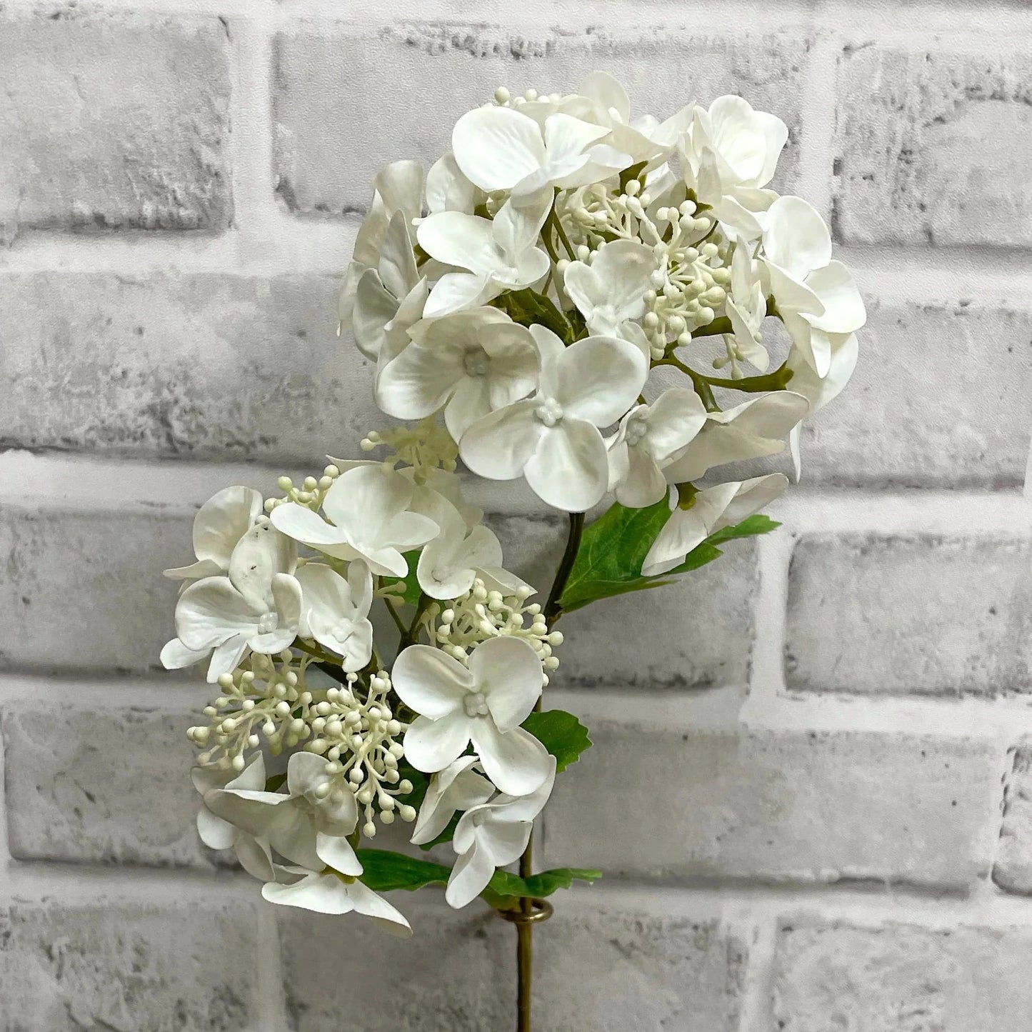 White hydrangea flower arrangement against a light gray brick wall