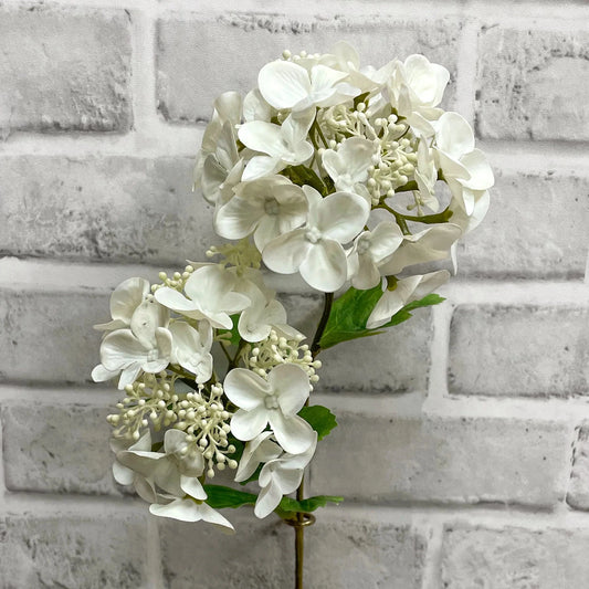 White hydrangea flower arrangement against a light gray brick wall