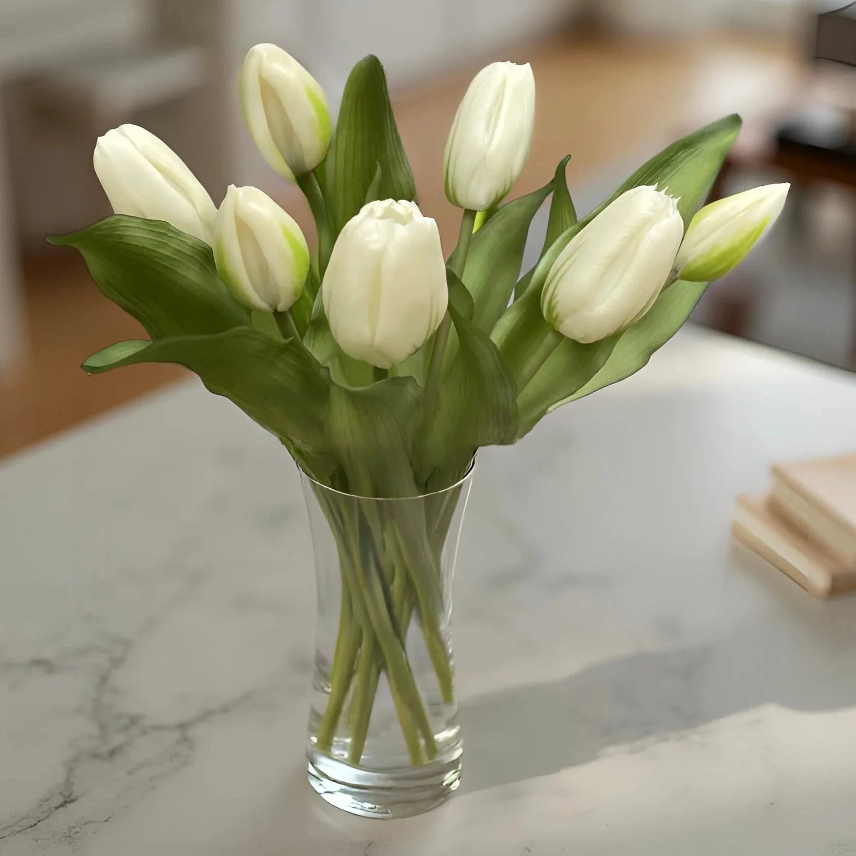 Clear glass vase with white tulips on a marble countertop